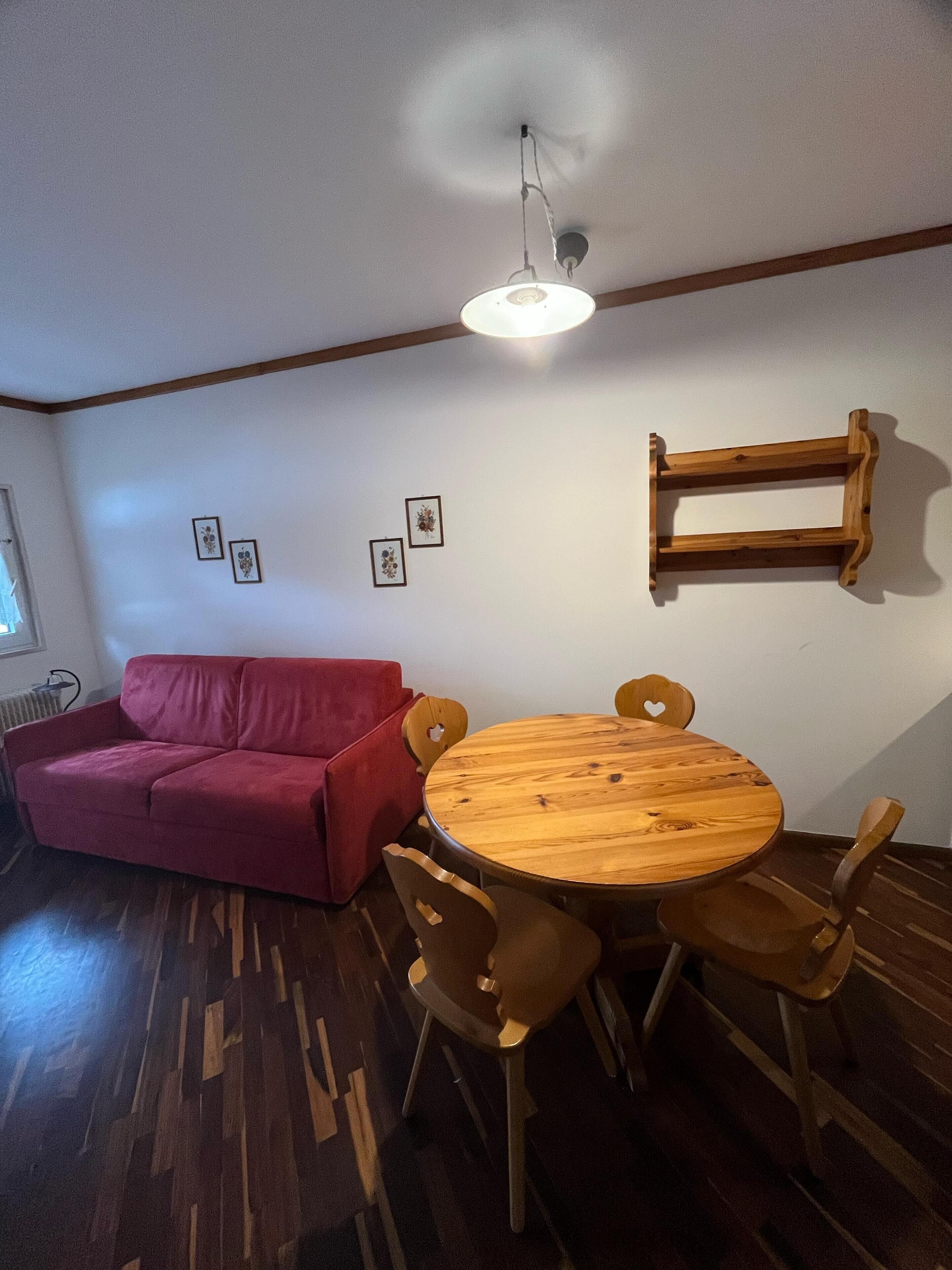 A room with a wooden dining table, four chairs, a red sofa, and a ceiling light fixture.