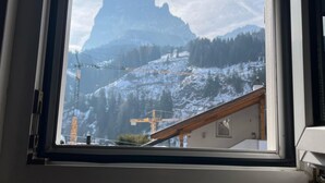 Une fenêtre donnant sur un paysage montagneux, avec notamment un sommet imposant et une grue de construction.