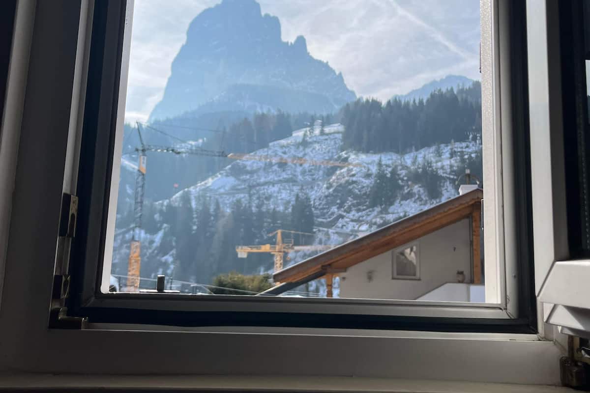 A window with a view of a mountainous landscape, including a prominent peak and a construction crane.