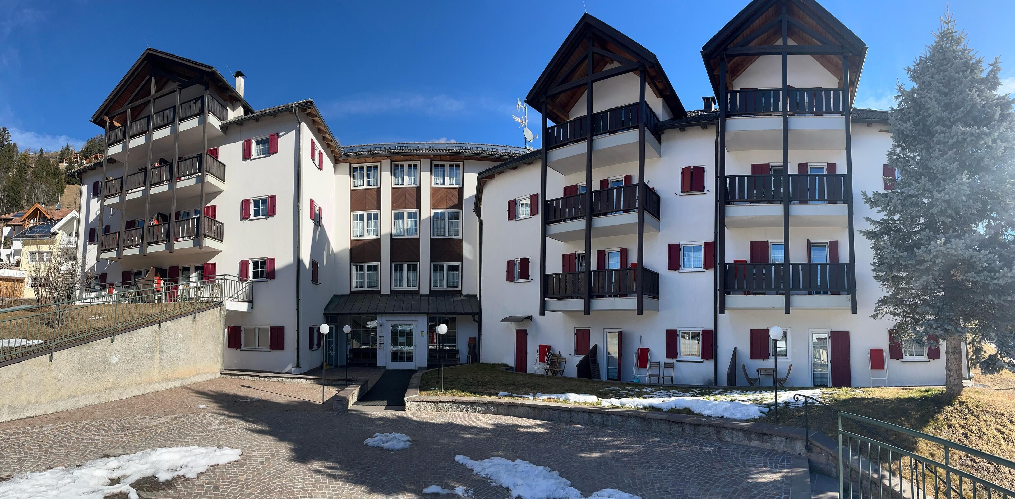 Un edificio de varios pisos con balcones, una entrada central y el suelo cubierto de nieve.