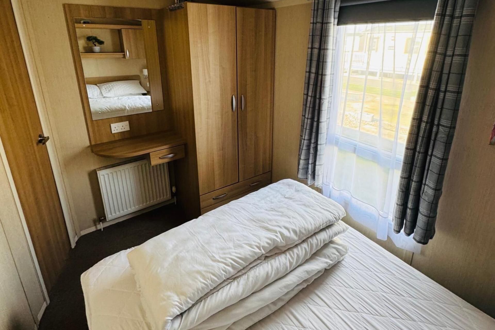 A compact bedroom with a single bed, wooden wardrobe, and a window with curtains.