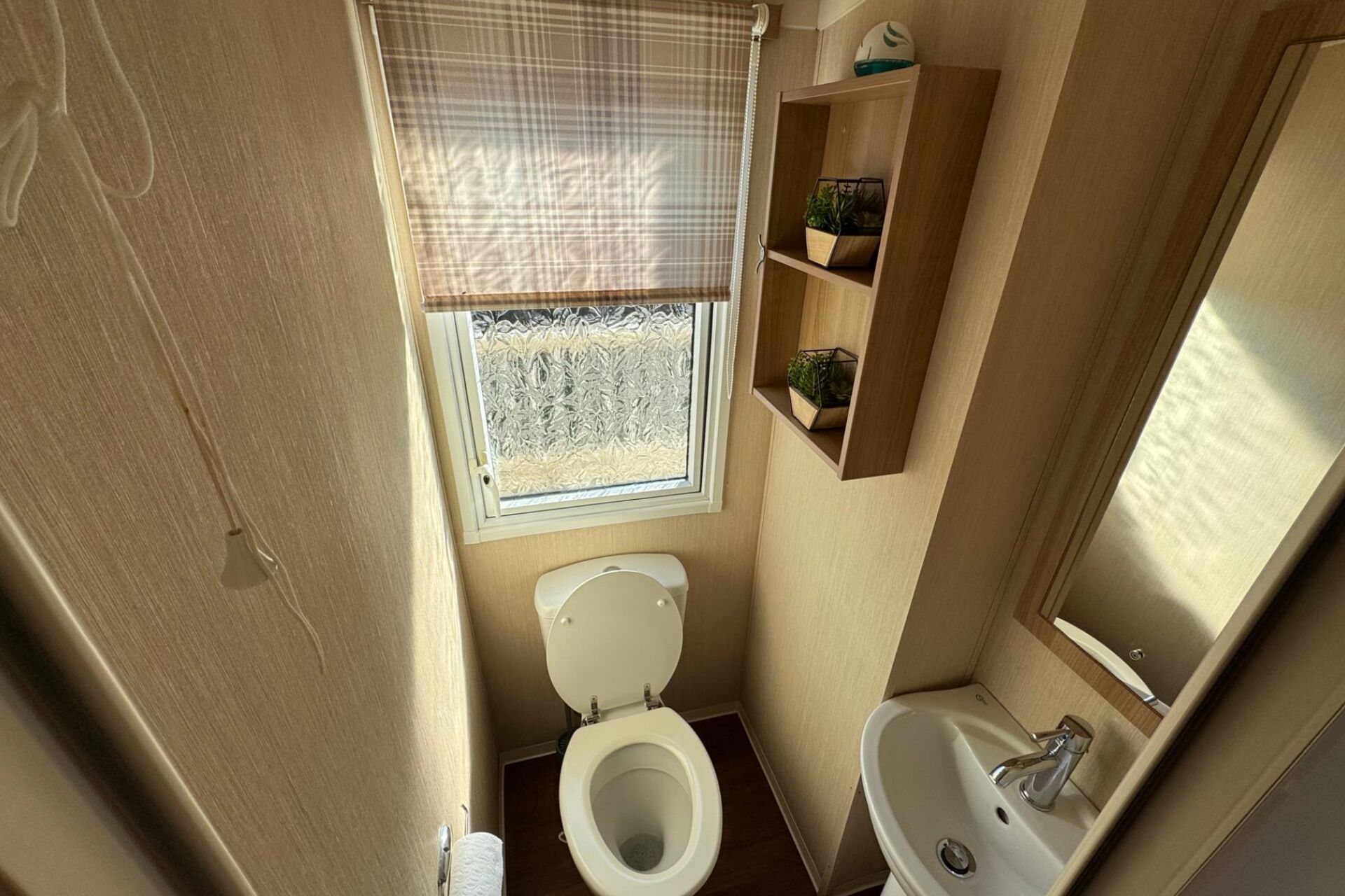 A compact bathroom with a toilet, sink, and window with frosted glass.