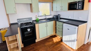 A compact kitchen with a stove, sink, microwave, and dishwasher. - Statichome-sleeps6-lakeview-balcony-parking-petsok (Mablethorpe)