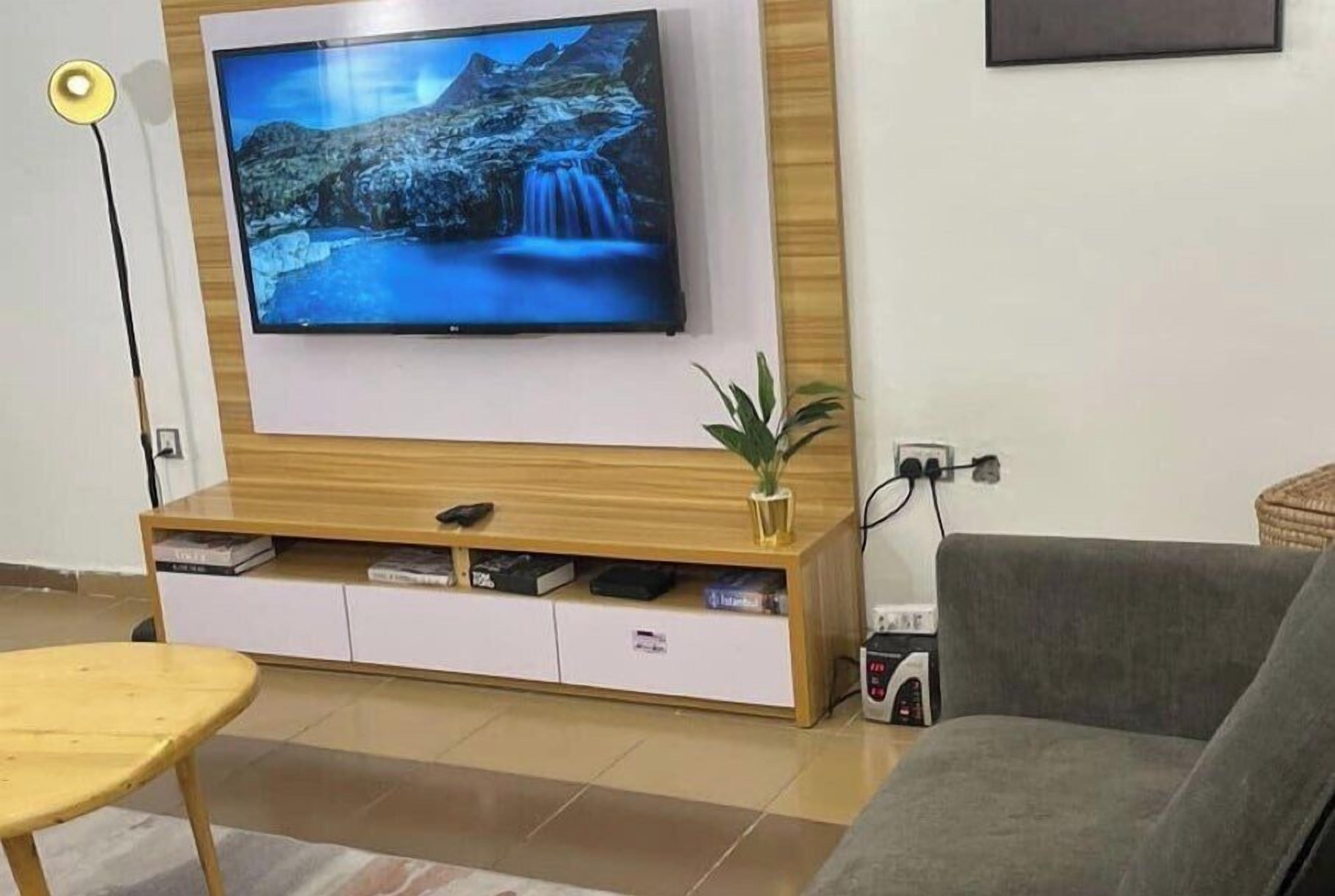 Una sala de estar con un televisor montado, un mueble de madera para entretenimiento, un sofá gris y una mesita.