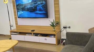 A living room with a mounted TV, a wooden entertainment unit, a grey sofa, and a small table.
