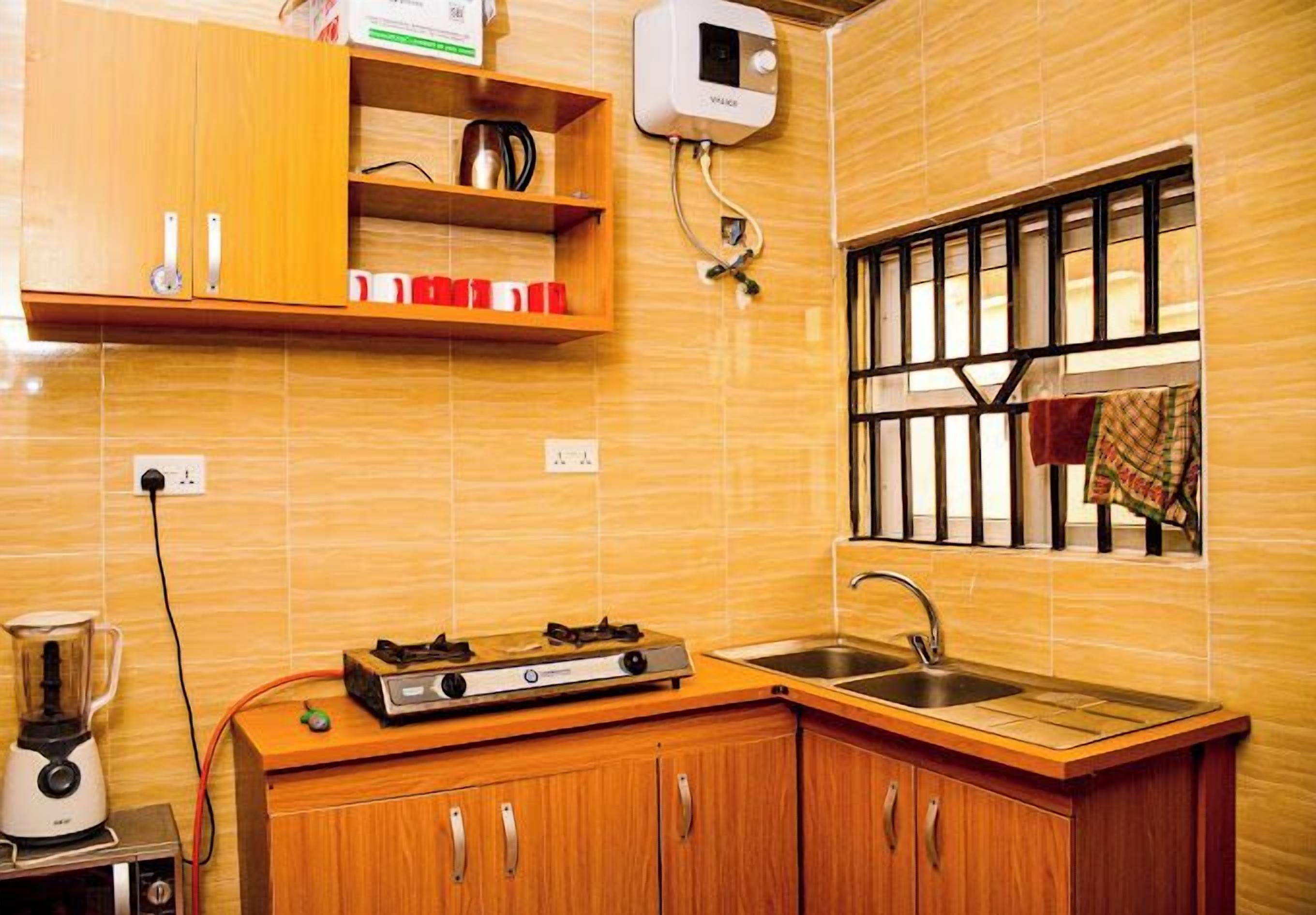 Cocina compacta con gabinetes de madera, estufa a gas, licuadora y una ventana con rejas.