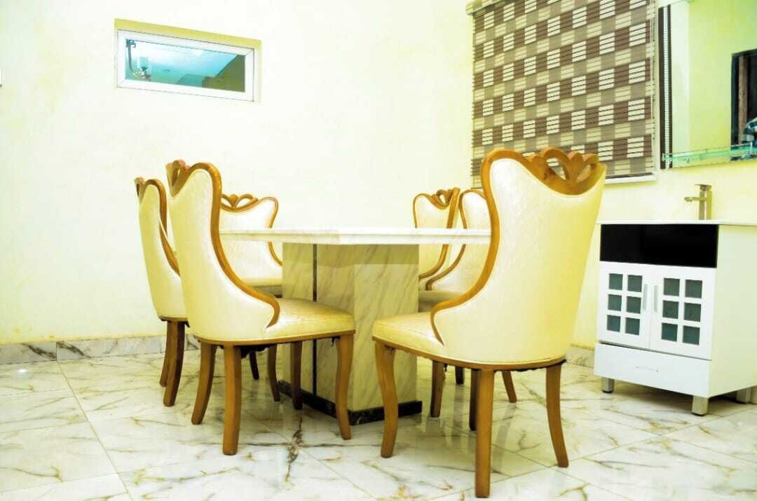 Un espace repas doté d’un sol en marbre, d’une table blanche et de quatre chaises aux pieds en bois et au dossier incurvé.