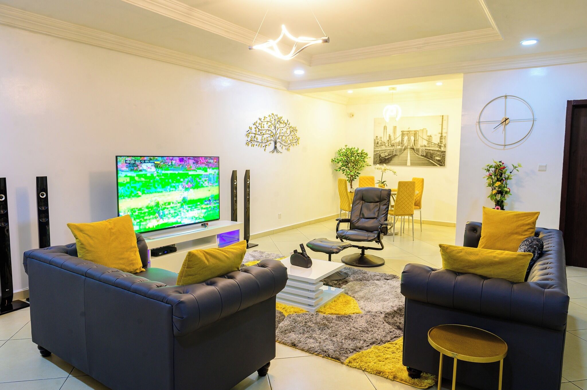 A modern living room with a flat-screen TV, two sofas with yellow cushions, a coffee table, and a small side table.