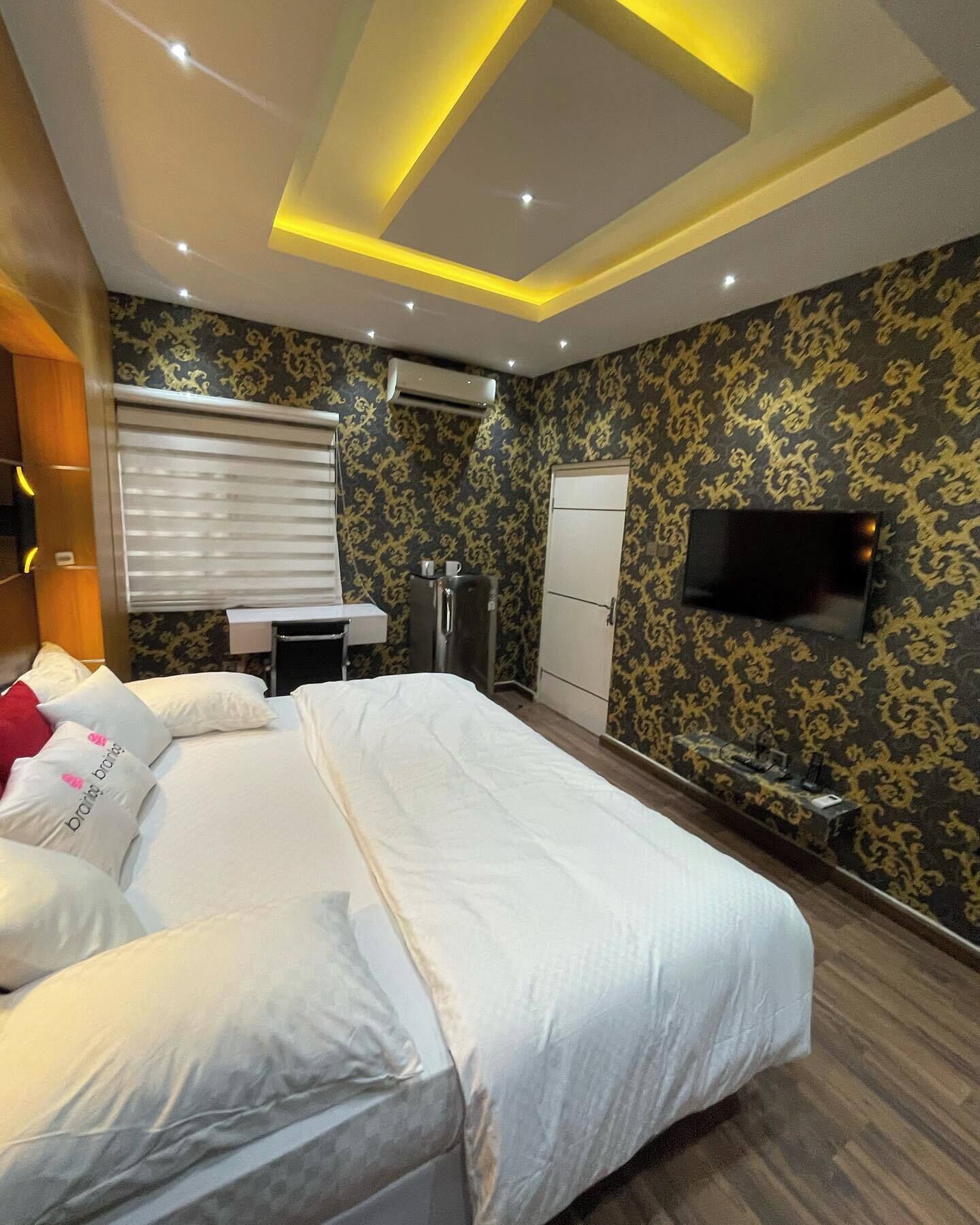 A hotel room with a large bed, a desk, a wardrobe, and a flat-screen TV mounted on the wall.