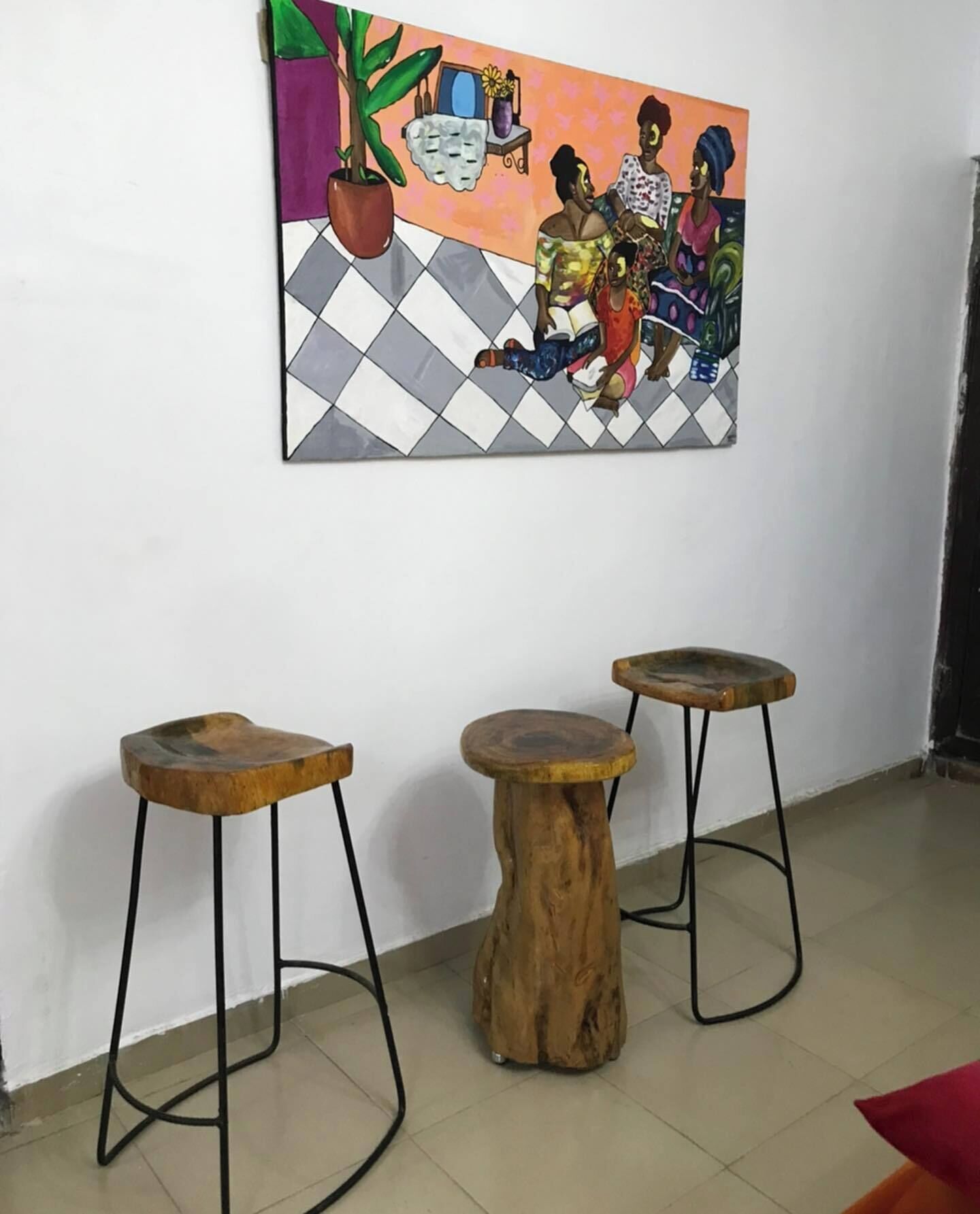 A room with three wooden stools, a large painting on the wall, and a potted plant.