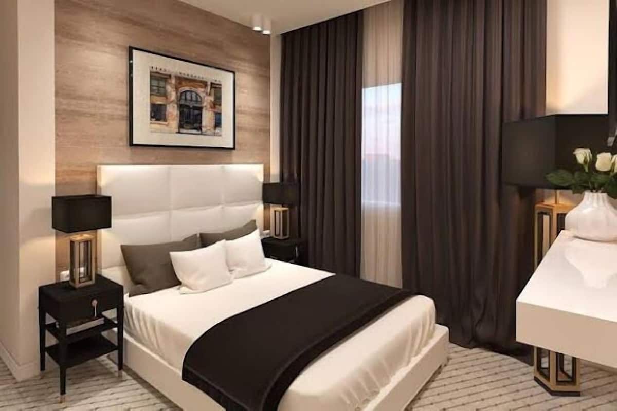 Quarto de hotel moderno com uma cama grande, duas mesas de cabeceira, uma escrivaninha e um quadro na parede.