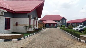 A building with red roofs and a gravel driveway leading to a parking area. - FFA RESORT CENTRE (Akure)