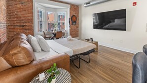 A modern living room with a leather sofa, a bed, a TV, and a brick wall.