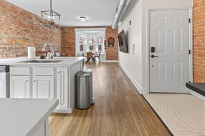 A kitchen with white cabinets, a stainless steel sink, and a trash can.