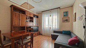 A living room with a wooden dining table, chairs, a sofa, and a television.
