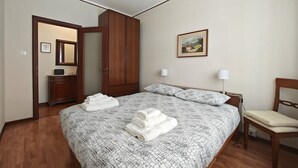 A bedroom with a large bed, wooden wardrobe, bedside lamps, and a painting on the wall.