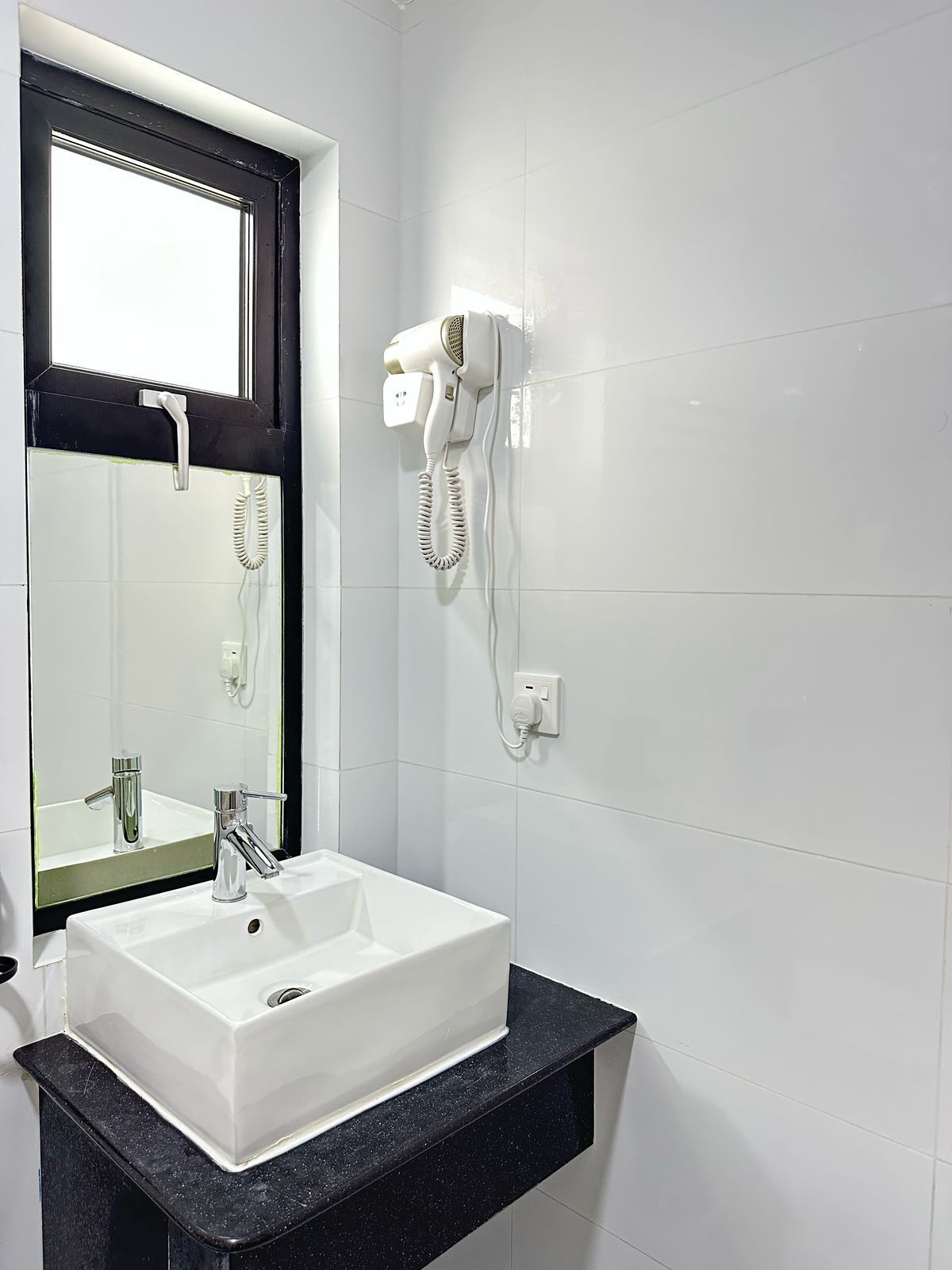 Un baño con un lavamanos blanco, un espejo y un secador de pelo montado en la pared.