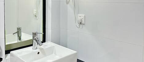 Un baño con un lavamanos blanco, un espejo y un secador de pelo montado en la pared.