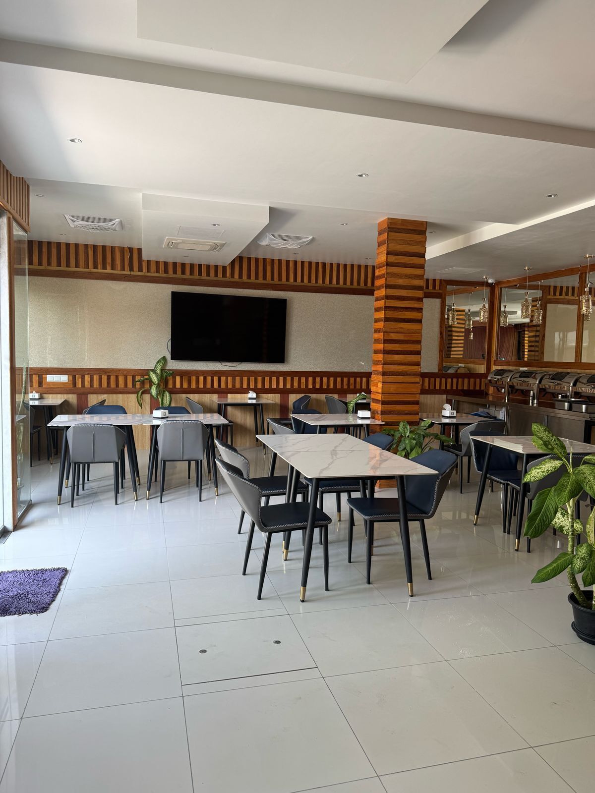 Un restaurante con varias mesas y sillas, un televisor de pantalla plana en la pared y un pilar de ladrillo.