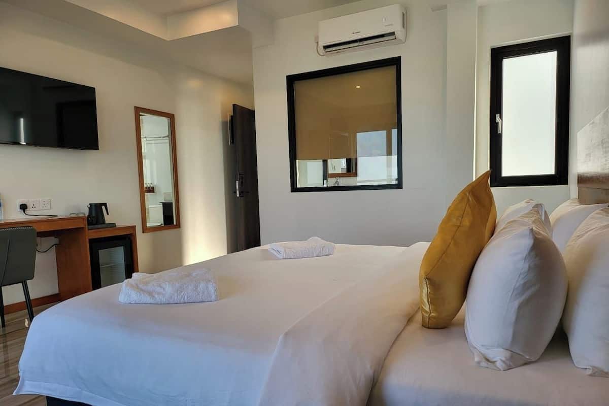 A hotel room with a large bed, a desk with a chair, a mirror, and an air conditioning unit.
