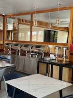 Un restaurante con una barra larga, varios dispensadores de bebidas, luces colgantes y un espejo grande.