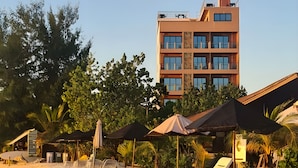 Un hotel frente a la playa con varios pisos, sombrillas exteriores y sillones de descanso.