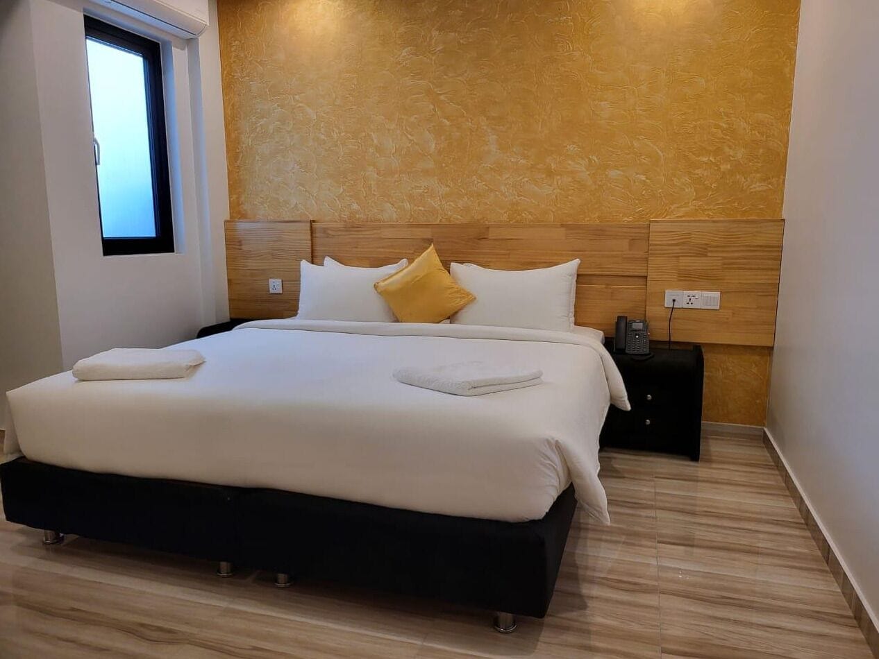 A modern bedroom with a large bed, wooden headboard, and a small bedside table with a phone.