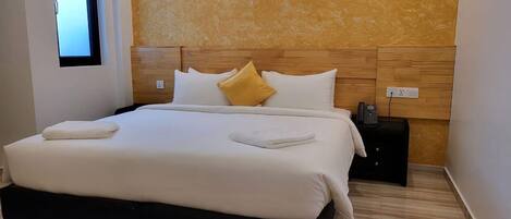 A modern bedroom with a large bed, wooden headboard, and a small bedside table with a phone.