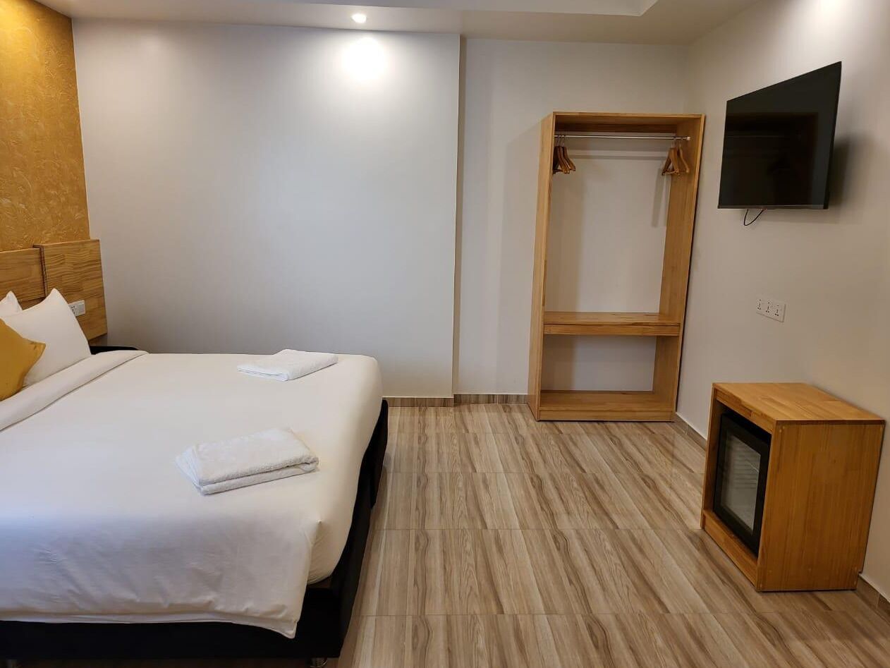 A hotel room with a bed, a wooden wardrobe, a television, and a small wooden cabinet.