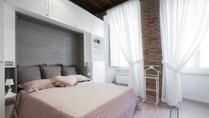 Un dormitorio con una cama grande, un armario, una mesita de noche y una pared de ladrillo.