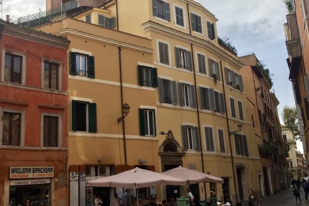 A street view with buildings, including a yellow building with green shutters and a sign for 'MACIERIA BIANCHERIA'.