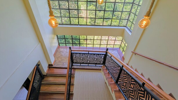 A staircase with patterned railings and wooden steps leading to a balcony with a view of greenery. - Hillsgate EXPERIENCE  (Nairobi)