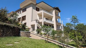 A multi-story residential building with a balcony on the second floor, a stone retaining wall, and a grassy area with trees. - Hillsgate EXPERIENCE  (Nairobi)