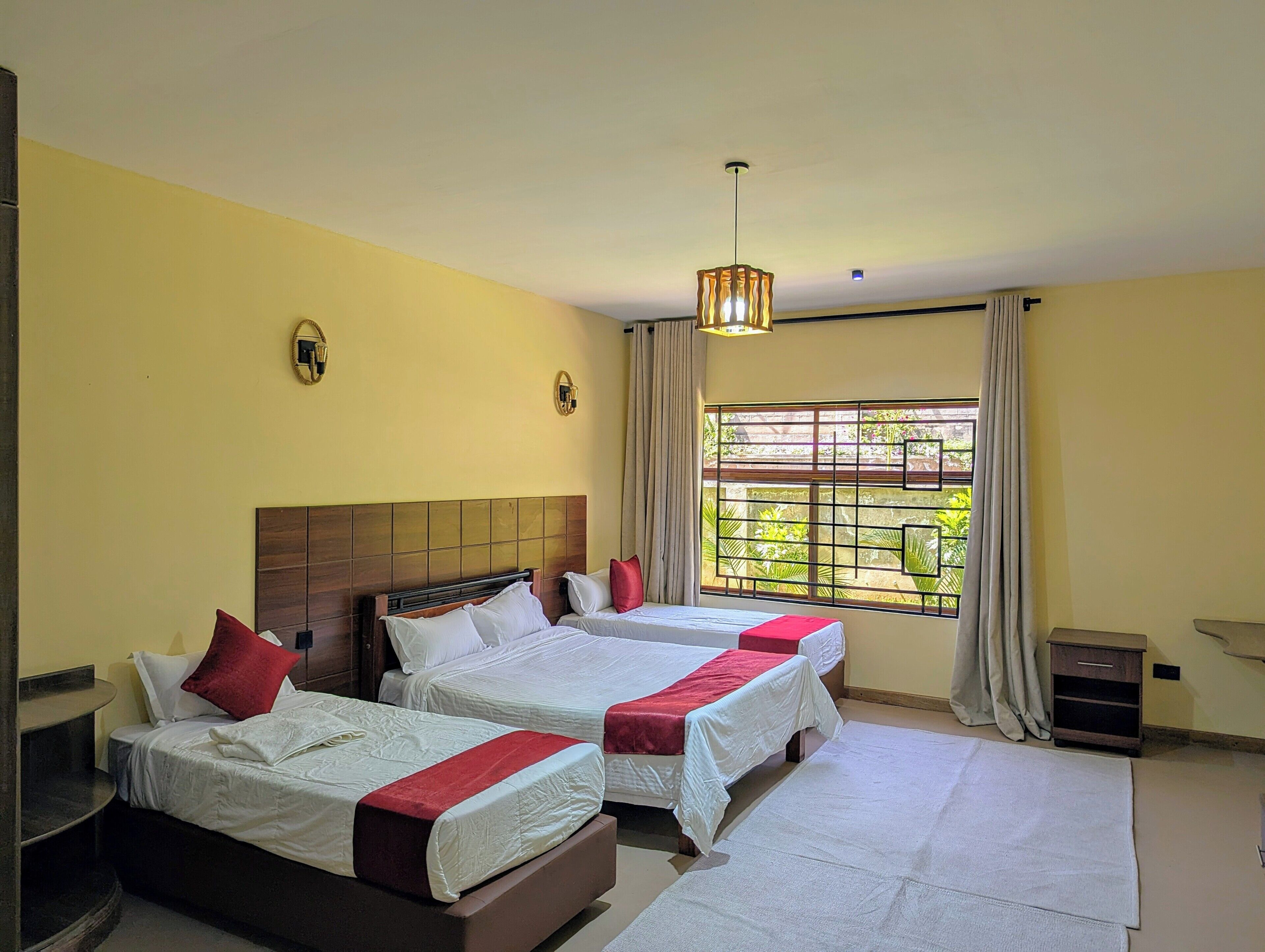 A hotel room with two beds, a window with a view, a small bedside table, and a hanging light fixture.