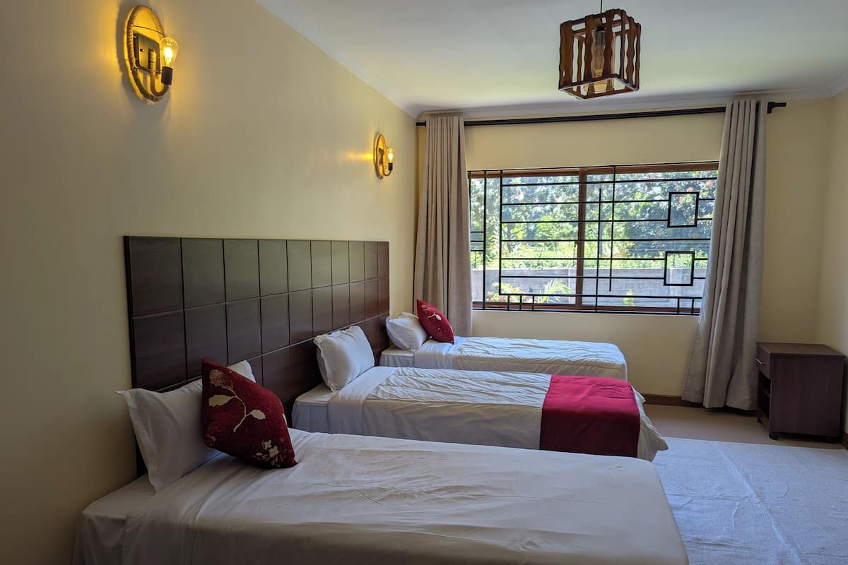 Habitación de hotel con dos camas, cabecera, ventana con cortinas y lámpara colgante.