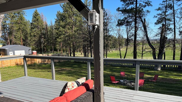 Une terrasse couverte, aménagée avec du mobilier d’extérieur, et offrant une vue sur une cour verdoyante avec des arbres.