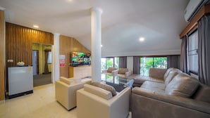 A modern living room with a sofa, armchairs, and a coffee table. There is a kitchen area in the background with a refrigerator and a TV. - Cozy gray garden (Pattaya)