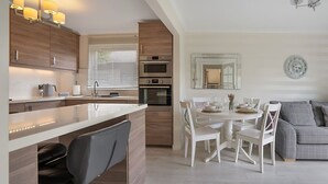 Une cuisine moderne dotée d’appareils électroménagers intégrés, un coin repas avec des meubles blancs et un canapé gris.