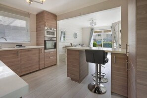 A modern kitchen with wooden cabinets, a built-in oven, and a bar area with a stool.