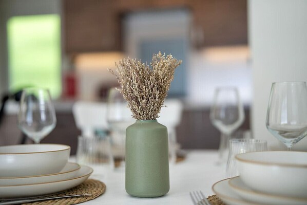 A dining table with a vase of dried flowers, white plates, and wine glasses.