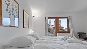 Un dormitorio con cama, almohadas, una silla y una ventana con vista a una torre.