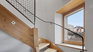 Una escalera de madera con barandilla de metal y ventana con vista a un muro de piedra.