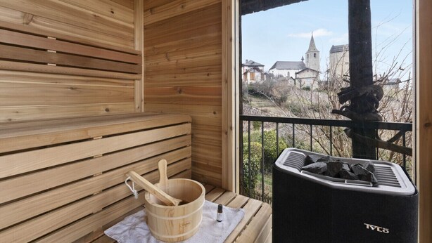 Una sauna de madera con un banco, un cubo de madera y un calentador de sauna negro.
