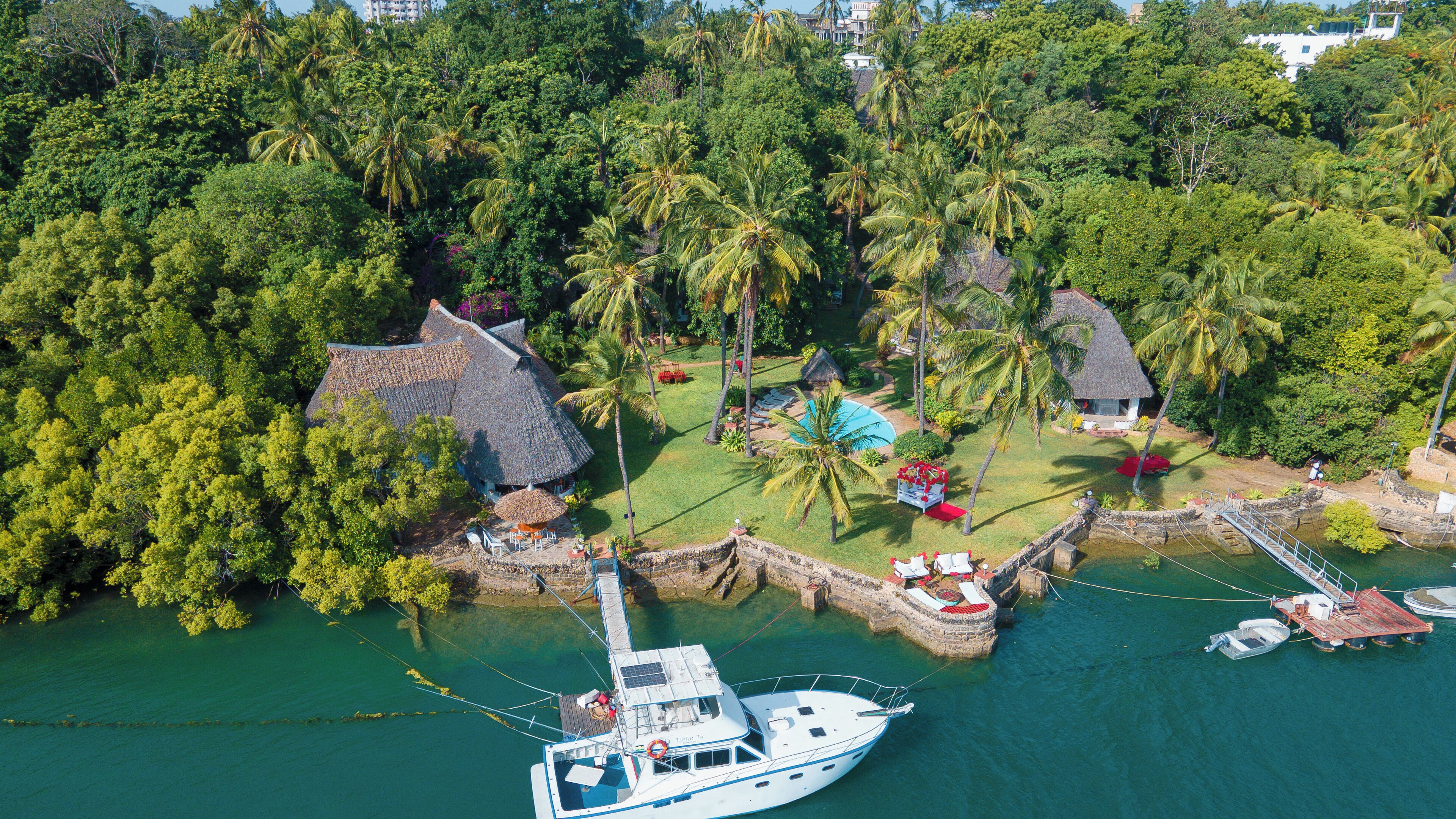 Ein Luftbild eines tropischen Resorts mit vertäutem Boot, einem Haus mit Strohdach und üppiger Vegetation.