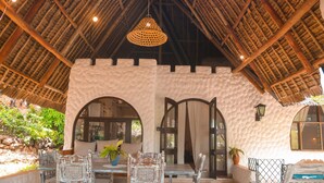 Un interior rústico con techo de paja alto, arcos y un comedor con sillas transparentes y una mesa.
