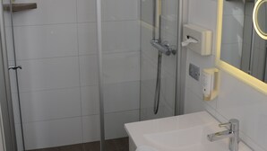 Une salle de bain moderne avec une douche à parois de verre, un lavabo blanc avec un miroir et une serviette accrochée au mur.