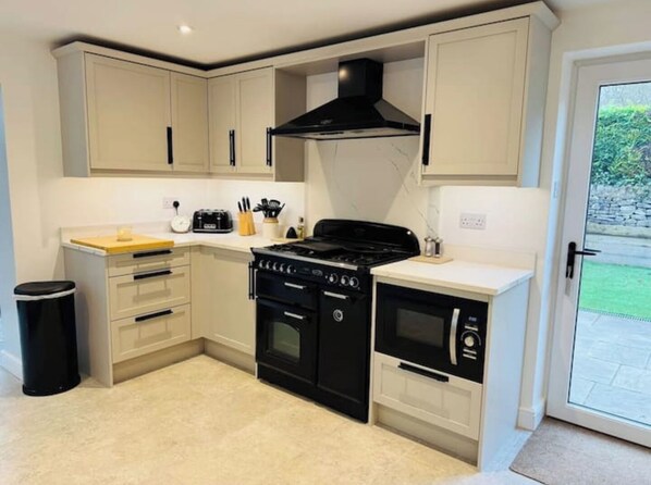 Compact kitchen with central gas stove, oven, and microwave, plus a toaster and knife block for meal preparation.