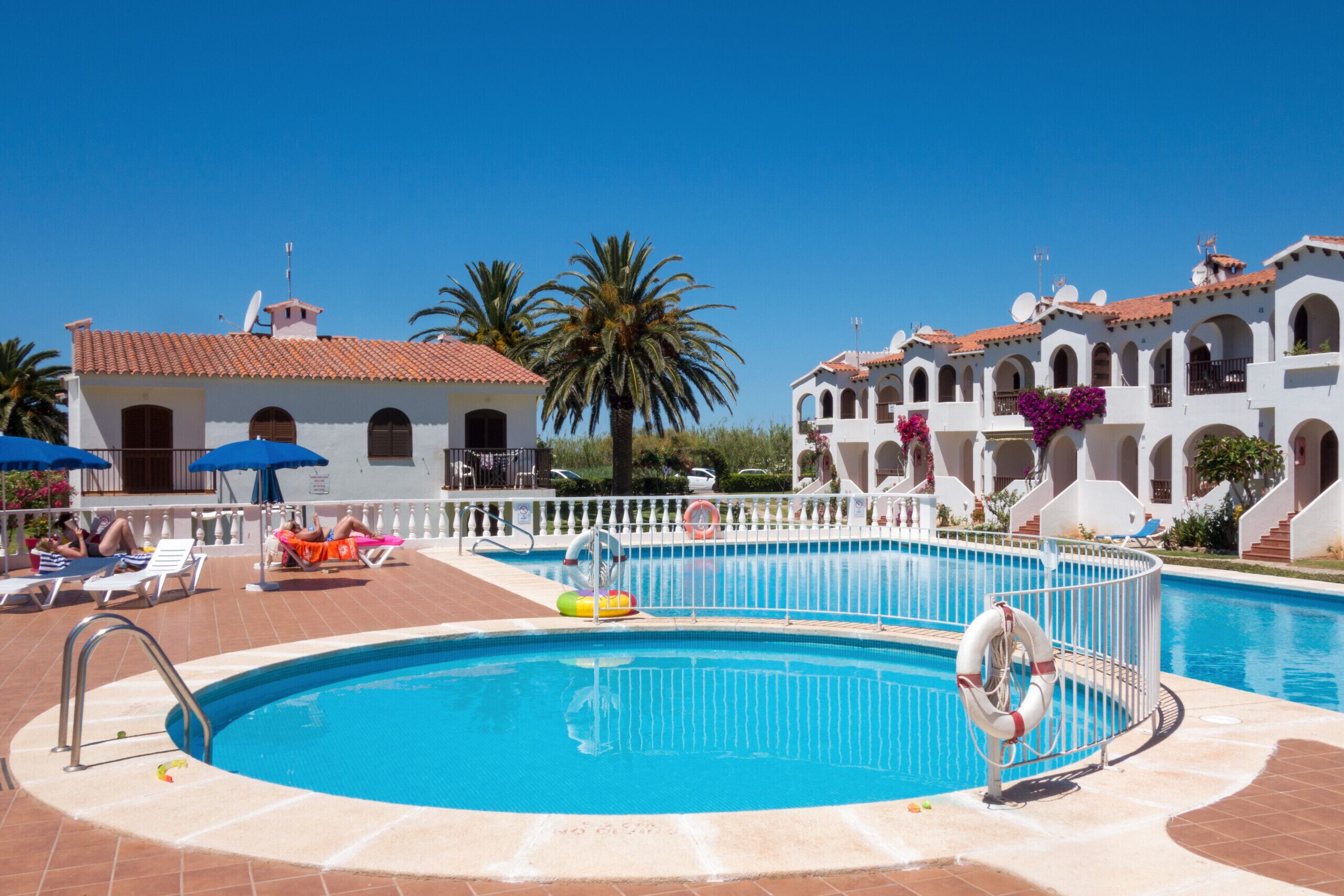 A pool area with lounge chairs, a lifebuoy, and a clear blue sky.