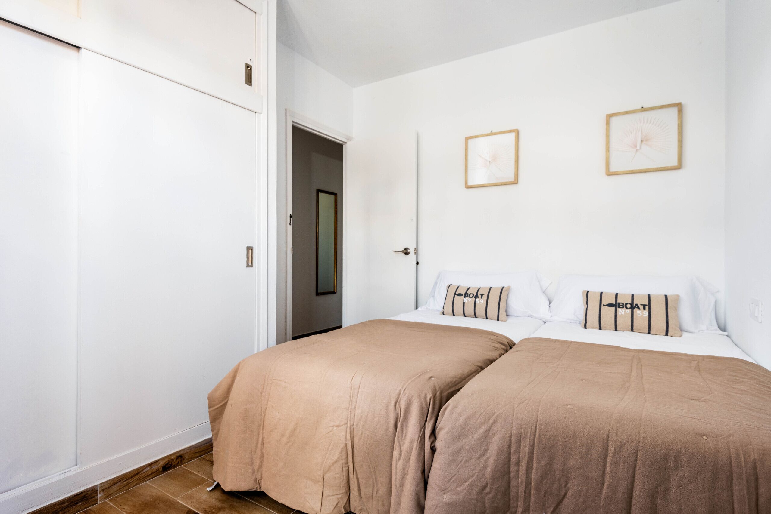 A bedroom with two beds, white walls, and a door leading to another room.