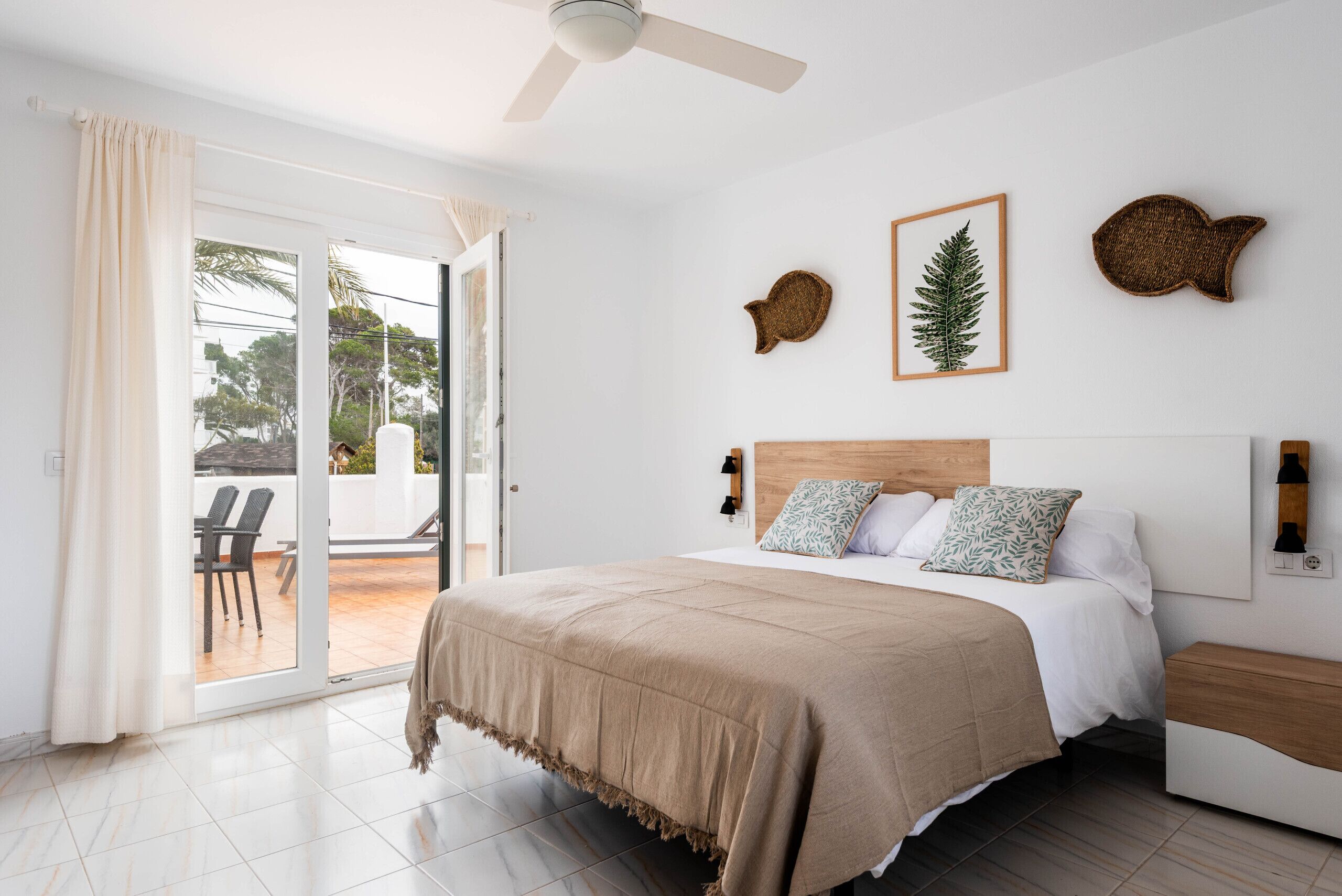Ein Schlafzimmer mit Bett, Deckenventilator, einer Glasschiebetür zum Patio und Wanddekoration.